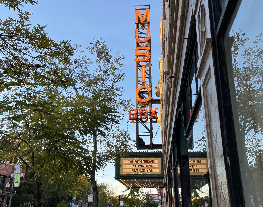 Chicago's Music Box Theater marquee. "Music Box" is spelled in red against a clear blue sky. The sign says "The 60th Chicago International Film Festival."